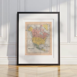 May include: Framed vintage map of North America, showing the continent in yellow, pink, and green. The map is in a black frame with a white mount. The framed map is suitable for home decor and measures approximately 61 x 46 cm.