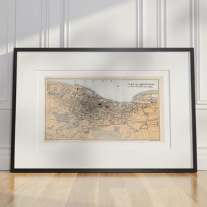 May include: Framed vintage map of Greenock, Scotland, in a black frame with a white mount. The map shows detailed street layouts and geographical features, with text reading "PLAN OF GREENOCK". The map is set against a light beige background.