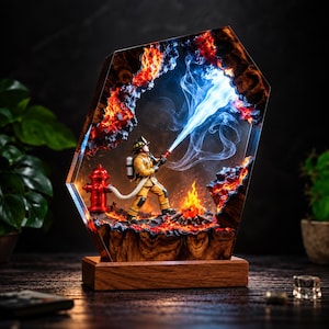 Könnte beinhalten: Eine dekorative Lampe aus Kunstharz und Holz mit einer Feuerwehrfigur in gelber Schutzkleidung, die einen blauen Lichtstrahl versprüht. Die Szene umfasst einen roten Hydranten, glühende Kohlen und verkohltes Gestein in einem Rahmen.