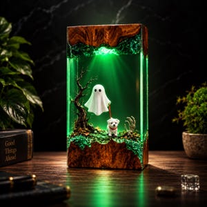 Può includere: Una lampada rettangolare con base e parte superiore in legno naturale e un centro in resina verde traslucida. All'interno, una figura di fantasma bianco tiene un guinzaglio rosso legato a un piccolo cane bianco, accanto a un albero e una mano scheletrica.