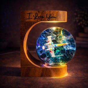 May include: A wooden night light with the text "I Love You" and a glass sphere containing a model airplane. The sphere has a blue and green galaxy design. The base and frame are made of wood.