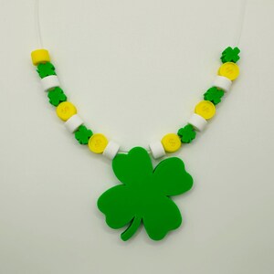 May include: A green four-leaf clover charm necklace with white and yellow beads. The necklace is made of plastic and is perfect for St. Patrick's Day.