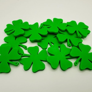 May include: A collection of bright green four-leaf clovers, a symbol of good luck. The clovers are scattered on a white surface, creating a festive and cheerful display. Ideal for St. Patrick's Day decorations or craft projects.