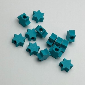 May include: A group of teal blue star-shaped beads with a hole in the center of each star. The beads are scattered on a white surface.