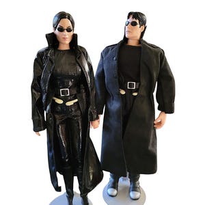 May include: Two action figures of characters from a movie, both wearing black outfits and sunglasses. The figure on the left has a shiny black coat, while the figure on the right has a matte black coat. Both figures are standing on gray circular bases.