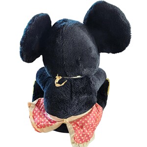 May include: A vintage black plush toy mouse with large, rounded ears. The mouse wears a pink and white polka-dot skirt with a cream-colored trim. The toy is viewed from the back, showcasing its plush texture and design.