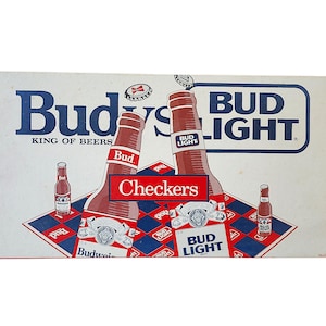 May include: Vintage Budweiser and Bud Light beer advertisement. The image features two large beer bottles with the words "Bud" and "Bud Light" in blue and red. The background has a checkerboard pattern in red, white, and blue.