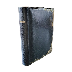 May include: A vintage, dark green leather-bound book with gold-colored filigree edging. The word "MISSEL" is printed in gold on the spine. The book has a textured surface and a zipper closure.