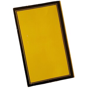 May include: A rectangular yellow object with a black border and a thin gold inner border. The object is slightly angled, showcasing its design against a white background. The yellow surface has a few small imperfections.