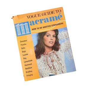 May include: A vintage instructional book titled Vogue Guide to Macramé: How to Do Knotted Stringwork. The orange and blue cover features a photograph of a person wearing a white knotted string top and a beaded necklace, with a list of projects.