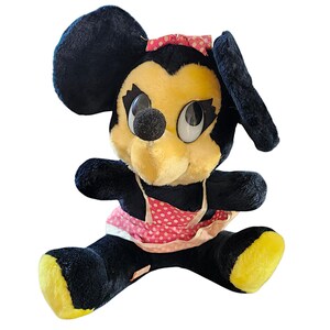 May include: Vintage Minnie Mouse plush toy. The plush features a black body, yellow face and feet, and a pink polka dot bow and apron. The toy has large, expressive eyes and a black nose.