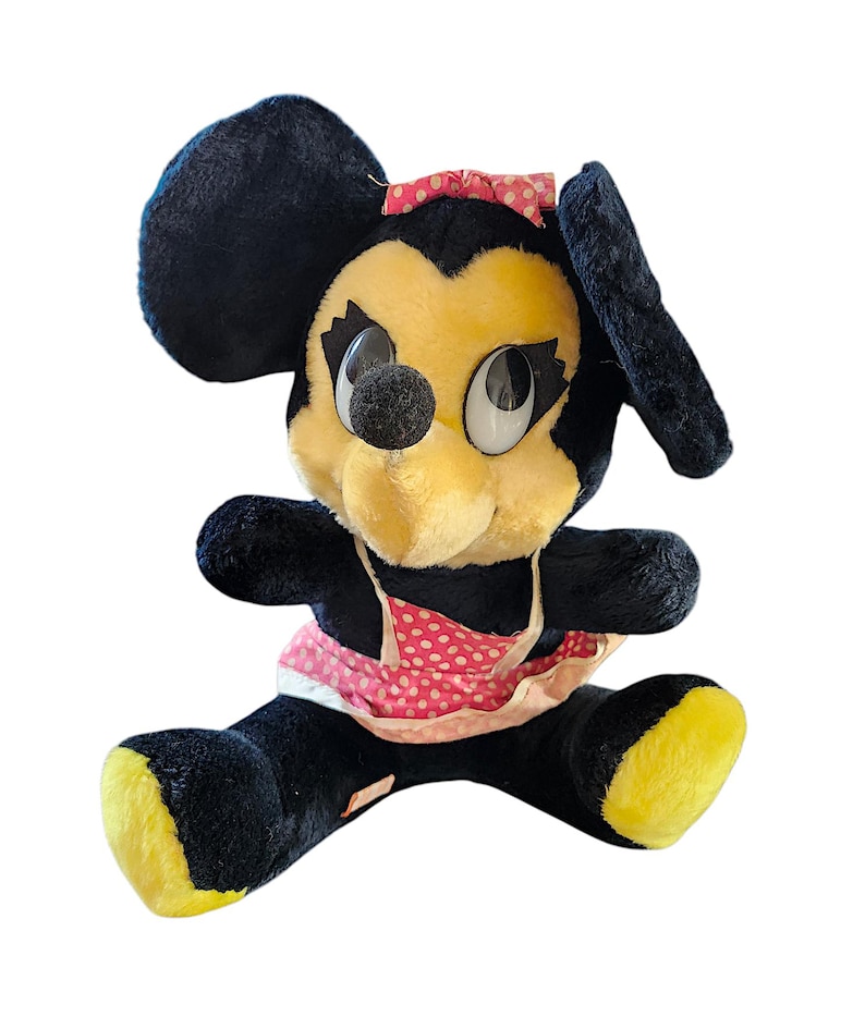 May include: Vintage Minnie Mouse plush toy. The plush features a black body, yellow face and feet, and a pink polka dot bow and apron. The toy has large, expressive eyes and a black nose.