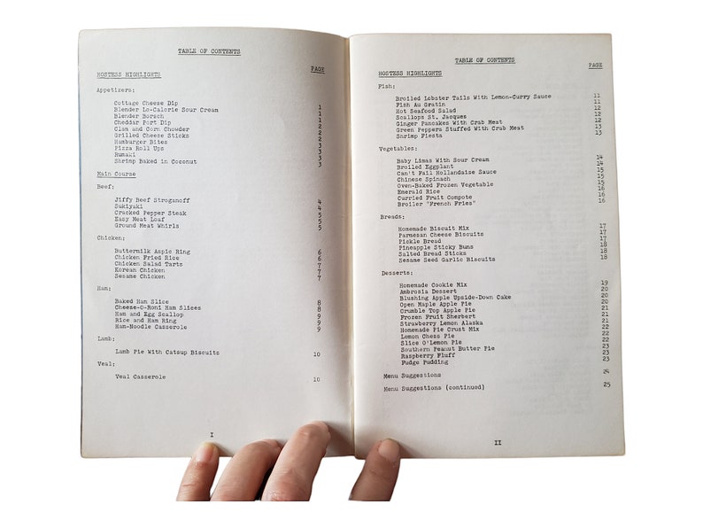 May include: An open cookbook showing two pages of a Table of Contents. The left page lists appetizers, beef, chicken, ham, lamb, and veal dishes. The right page lists fish, vegetables, breads, desserts, and menu suggestions with corresponding page numbers.