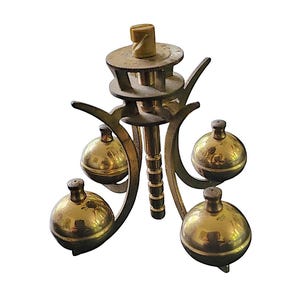 May include: A vintage brass clock pendulum with four spherical weights. The pendulum has a central rod with a threaded top and a wooden adjustment knob. The weights are evenly spaced around the central rod, creating a balanced design.