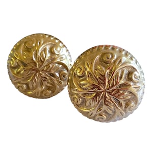 May include: A pair of gold-colored, round earrings. Each earring features an embossed floral design with intricate details. The earrings have a textured surface and a classic, vintage aesthetic.