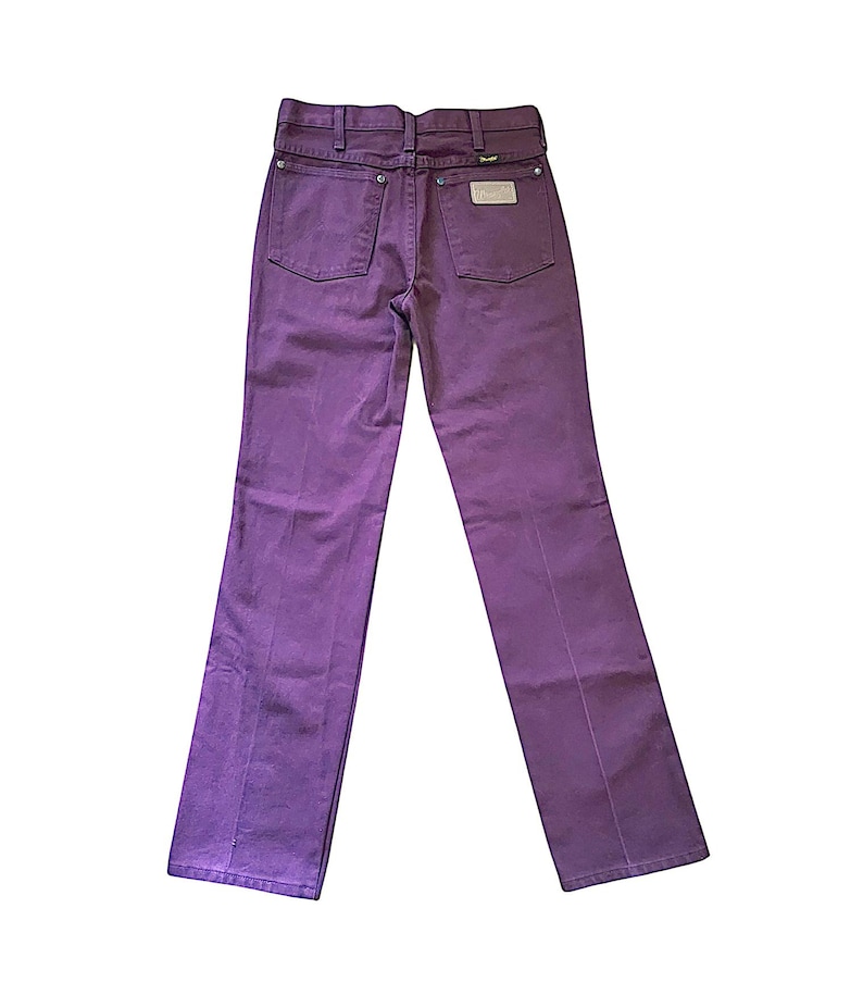 Puede incluir: Unos pantalones vaqueros de color morado con dise&ntilde;o de cintura alta, trabillas para cintur&oacute;n, dos bolsillos traseros y remaches met&aacute;licos plateados. Una etiqueta rectangular blanca de la marca est&aacute; cosida en el bolsillo trasero derecho.
