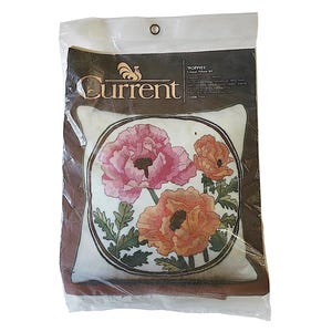 May include: A Current brand Poppies crewel pillow kit in a clear plastic package. The kit features a printed design of pink and orange poppies on a white background, enclosed in a dark brown oval border. Text on the package includes Poppies Crewel Pillow Kit and Code 7133.