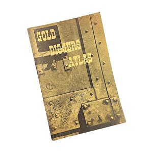 May include: A vintage book titled "Gold Diggers Atlas" with a weathered, textured cover. The cover is a mix of brown and gold tones, with the title in bold, block letters. The design resembles a metal door with rivets and a keyhole.
