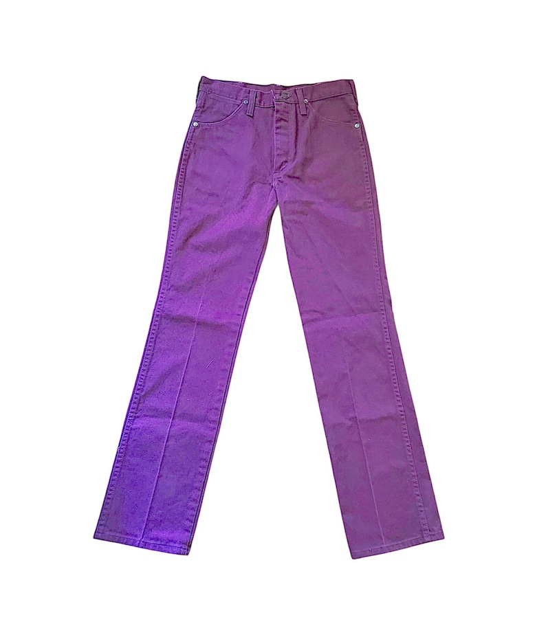 Puede incluir: Unos pantalones vaqueros de color morado s&oacute;lido con dise&ntilde;o de cintura alta, cierre de bot&oacute;n y cremallera, cinco bolsillos y perneras rectas con costuras verticales visibles a lo largo de la parte delantera de cada pierna, sobre fondo blanco.