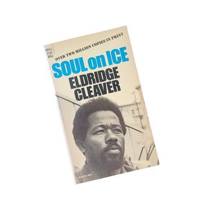 May include: Vintage paperback book titled "Soul on Ice" by Eldridge Cleaver. The cover features a black and white portrait of the author and the title in blue and black text. The book is a Dell paperback.