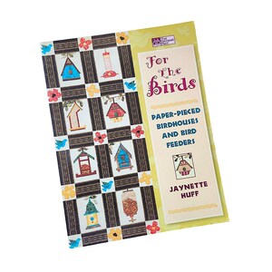 May include: A softcover instructional book titled For The Birds: Paper-Pieced Birdhouses and Bird Feeders by Jaynette Huff. The cover features a quilt pattern with various birdhouse and bird feeder designs, yellow flowers, and blue birds.