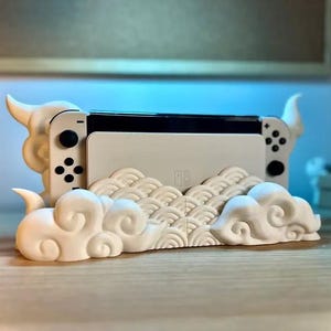 Könnte beinhalten: Ein weißer Nintendo Switch Konsolenständer mit einem Wolken- und Wellendesign. Der Ständer ist aus Kunststoff und hat einen Ausschnitt für die Controller der Konsole.