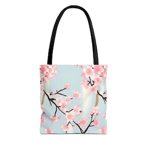 May include: A light blue tote bag with a floral print of pink cherry blossoms on branches. The bag has black handles.