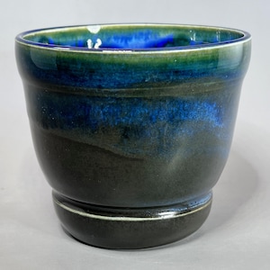 May include: A dark green ceramic planter with a blue and green glaze. The planter has a wide base and a rounded shape.