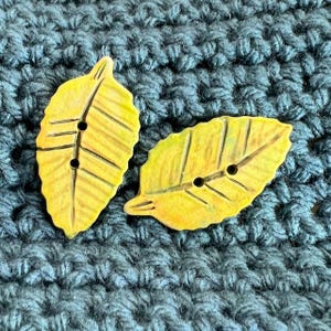 May include: Two yellow ceramic leaf-shaped buttons with a textured surface and two holes each.