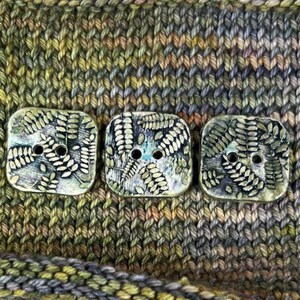 May include: Three square ceramic buttons with a fern leaf design in shades of green and gold. The buttons have two holes each.