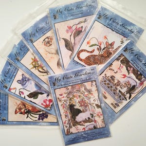 May include: A collection of "My Cats Garden" quilt block patterns. Each pattern features a different cat breed with floral accents. The patterns are packaged in clear plastic sleeves, with text including breed names like "Abyssinian" and "Egyptian Mau".