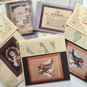 May include: A collection of cross-stitch pattern booklets featuring various designs including an angel in a flowing dress, a gazebo scene, a floral wreath, and a sampler with the text The birds go to sleep By the sweet wild twist of her song.