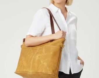 May include: A mustard-colored tote bag with brown leather straps. The bag has a rectangular shape with a textured appearance and a side pocket. The bag is carried over the shoulder.