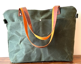 May include: A dark green canvas tote bag with two brown leather straps. The straps are stitched together with a yellow thread.