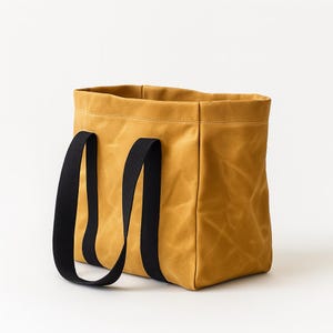 May include: Mustard-colored tote bag with black handles. The bag is made of a sturdy, textured material and has a rectangular shape. The black handles are attached to the sides of the bag and are long enough to be carried over the shoulder.