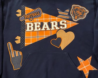 May include: Navy blue hooded sweatshirt with a front pocket, decorated with orange and white plaid and polka dot accents. The word "BEARS" is prominently displayed, along with a bear head and football graphic.