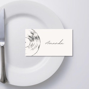 May include: A white place setting with a fork, knife, and a place card. The place card features a black and white vinyl record design and the name "Amanda" in script.