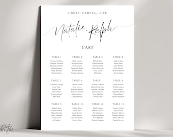 May include: A minimalist wedding seating plan featuring the names "Natalie" and "Ralph" in elegant script. The words "LIGHTS, CAMERA, LOVE" and "CAST" are above and below the names. Twelve tables are listed with guest names.