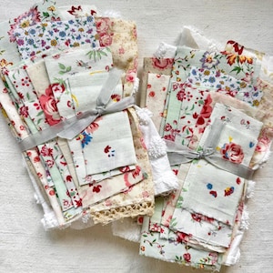 Puede incluir: Dos paquetes de retazos de tela variados con diversos estampados florales en tonos rojo, rosa, azul, verde y crema. Cada pila está atada con una cinta gris claro e incluye piezas con diferentes texturas, incluyendo adornos de encaje.