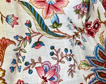 Puede incluir: Primer plano de una tela color crema con un estampado floral. El diseño presenta grandes flores rosas, azules y amarillas con tallos y hojas verdes y marrones. La tela tiene un aspecto texturizado.