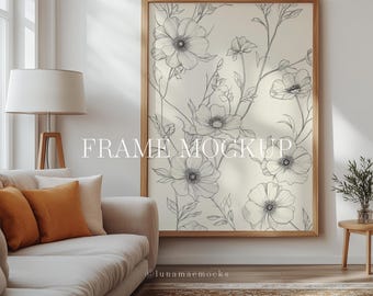 May include: A framed print of a black and white floral illustration. The print is in a light wood frame and is hanging on a white wall. The print is in a living room setting with a couch and a lamp.