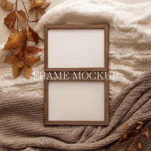 May include: Two wooden picture frames with white interiors are stacked on top of each other. The frames are surrounded by a cozy, neutral-toned blanket and autumn leaves. The text "FRAME MOCKUP" is displayed across the frames.