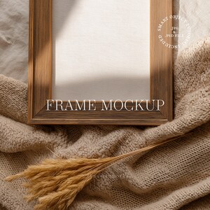 May include: A wooden frame mockup with the text "FRAME MOCKUP" in a serif font. The frame is brown and rests on a beige knitted blanket. A bundle of dried wheat is in the foreground. The image includes a "SMART OBJECT" label.