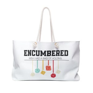 May include: A white tote bag with rope handles featuring the black text ENCUMBERED and WISH I HAD A BAG OF HOLDING. Below the text are colorful illustrations of various polyhedral dice hanging from thin lines in shades of red, blue, and yellow.