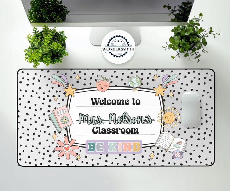 May include: A rectangular desk mat with a black and white polka dot pattern. The mat features the text "Welcome to Mrs. Nelson's Classroom" and "BE KIND" in a colorful design, along with illustrations of a book, sun, and other graphics.