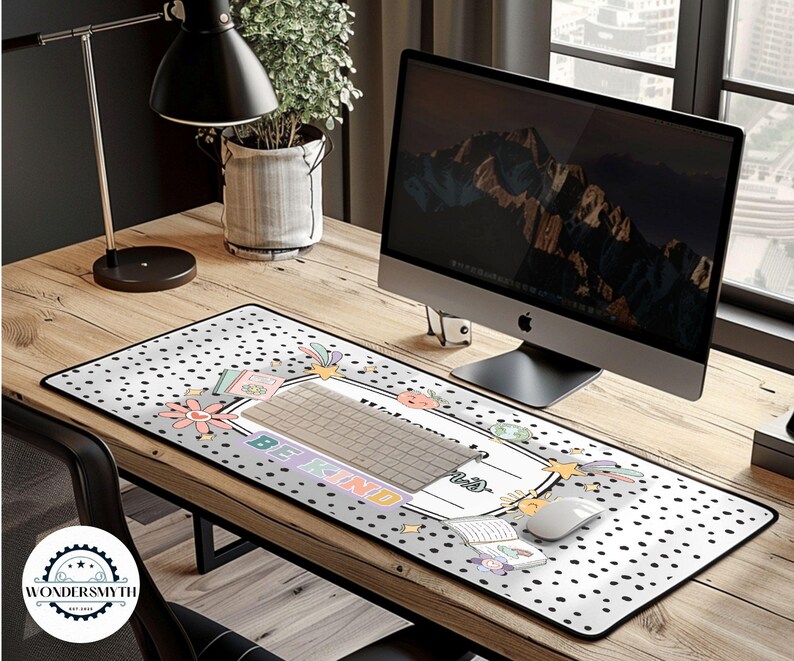 May include: A rectangular desk mat with a white background and black polka dots. The mat features a keyboard area with the words "BE KIND" and floral and pastel graphics. A computer mouse and keyboard are on the mat.