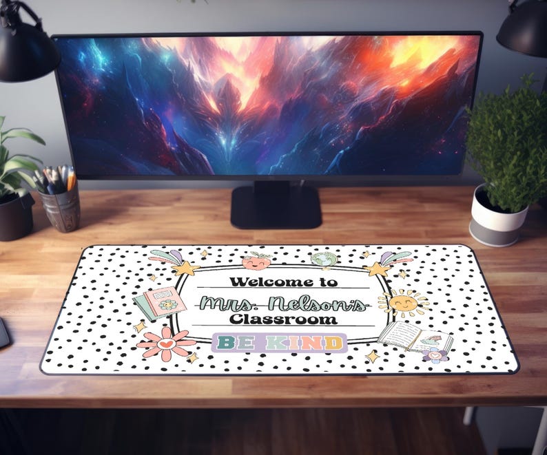 May include: A rectangular desk mat with a black and white polka dot pattern. The mat features the text "Welcome to Mrs. Nelson's Classroom" and "BE KIND" in a colorful, playful design. Decorative elements include flowers, books, and a sun.