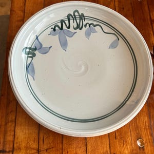 May include: A white ceramic serving platter with a green and blue floral design. The platter has a slightly raised rim and a smooth, glazed surface.