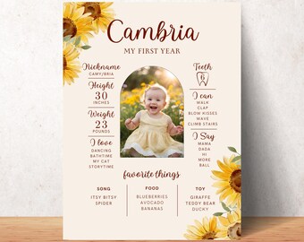 May include: A yellow and white baby milestone poster with sunflowers and a photo of a baby girl. The poster includes the baby's name, Cambria, and details about their first year, including height, weight, favorite things, and milestones.