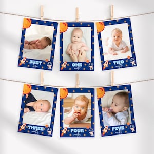 May include: Six baby milestone photo cards, each with a baby photo in a navy blue frame adorned with stars, a sun, a rocket, and an astronaut. The cards are strung on a clothesline and held by wooden pegs.